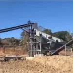 Heavy-duty gravel screening equipment working downstream from a rock grinder machine at an open-pit site.